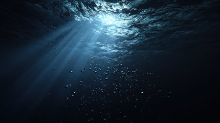 This image presents an underwater perspective, showcasing the interplay of light and water. Shafts of sunlight pierce through the water, creating a visually dynamic effect. The scene is dominated by deep blues and shadowy tones, with visible bubbles adding texture. Suitable for various conceptual and artistic applications, including designs and editorial projects.の素材
