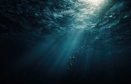 An underwater perspective reveals deep blue hues and textured water. Sunlight streams illuminate the scene, creating a dramatic effect. Bubbles rise towards the surface. This image is suitable for use in various projects, including educational materials, artistic endeavors, and commercial applications.の素材