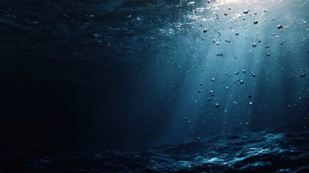 This underwater scene captures a tranquil moment with sunlight piercing through the surface. Bubbles float upward, adding texture to the water. The dark blue hues create an atmospheric environment. The image is suitable for various applications, including editorial content or commercial projects focused on nature.の素材