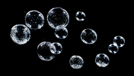 Multiple spherical, transparent bubbles float against a dark backdrop. Each bubble reflects light, creating highlights and a sense of depth. The composition is simple with focus on the bubbles. Suitable for various projects, including abstract concepts and visual enhancements, ideal for commercial uses.の素材
