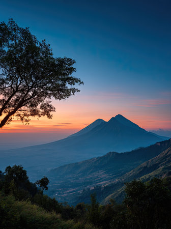 The image features a mountain range at dusk, under a vibrant sky displaying shades of orange and blue. A tree is positioned on the left side of the frame. This scene utilizes a gradient effect and is likely set outdoors, capturing a moment of natural beauty for various purposes.の素材