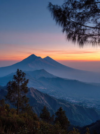 The image features a mountain range silhouetted against a vibrant sunset. The sky displays hues of orange and blue. The composition, taken from an elevated perspective, shows a clear view, possibly suitable for promotional materials or editorial features. The lighting is natural.の素材