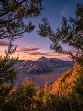 An aerial perspective captures a mountain range during sunset. The image displays a vibrant sky with shades of orange and purple. Lush greenery frames the central valley and mountain, with warm sunlight illuminating the foreground. This visual is suitable for various commercial applications including travel and nature themes.の素材