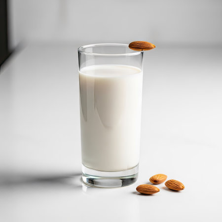 A close-up view displays a glass of almond milk and scattered almonds. The composition features a clear glass filled with white liquid. The setting appears to be indoors with soft, diffused lighting. This image is suitable for various commercial uses, including advertising and editorial content.の素材