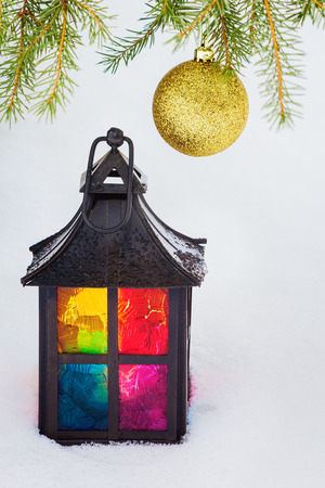 Multicolored decorative lantern in the snow and fur-tree branch with  Christmas ballの写真素材