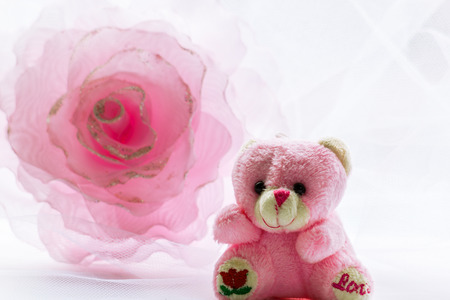 Pink flower decoration and teddy bear  against a white openwork fabricの写真素材