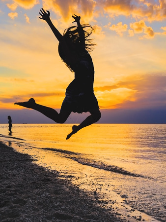 Silhouette of a girl jumping in the sea at sunsetの写真素材