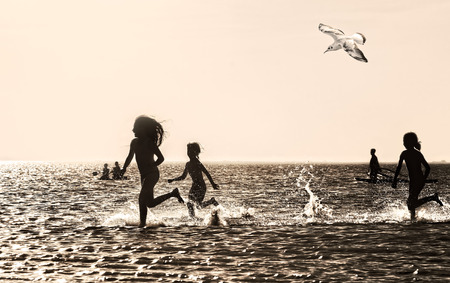 Silhouettes of children running through the water at sunset, backlit. Sepiaの写真素材