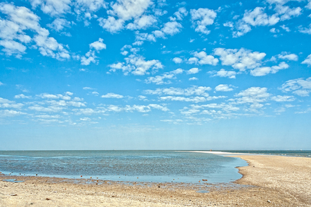 Deserted beach on a background of blue sky with white clouds on a summer morning