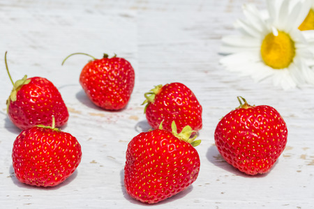 Ripe red strawberries on blurred background of white daisies, close-up. Selective focusの写真素材