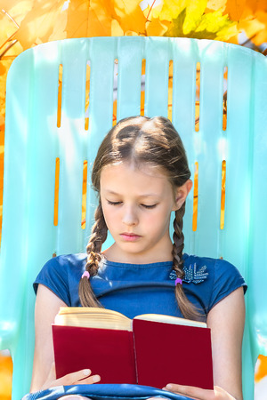 Girl sitting in a deck chair and reading a book in the garden on a sunny autumn dayの写真素材