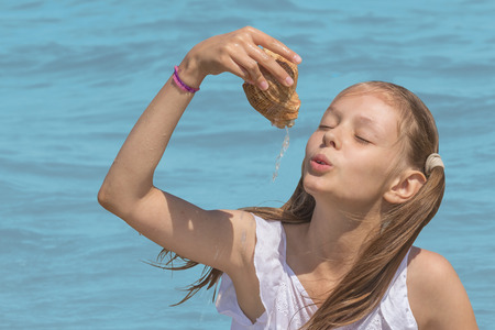 Girl in white dress plays with the shell on the background the turquoise seaの写真素材