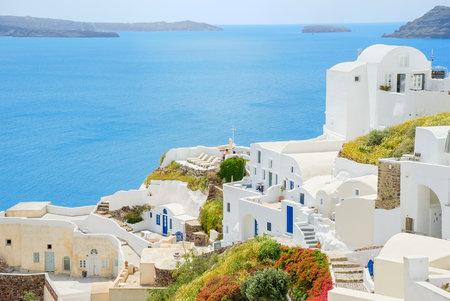 White town on the blossoming steep coast of the Greek island of Santorini on the background of blue sea and skyの写真素材