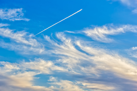 Blue sky with light white cirrus clouds and contrails at sunsetの写真素材