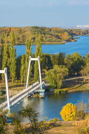 River landscape with a white cable-stayed bridge and a picturesque park on a sunny autumn dayの写真素材