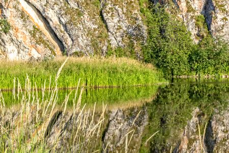 Scenic landscape with rock and reflection in the river on a quiet sunny summer evening, close-upの写真素材
