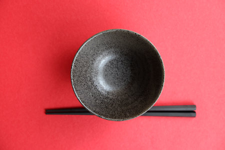 Empty black bowl and chopsticks on red background. Top view.の写真素材