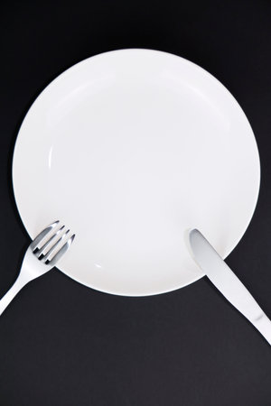 Empty white plate with fork and knife on black background, top viewの写真素材