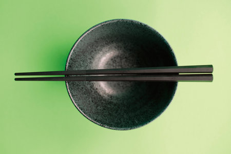 Black chopsticks in a bowl on a green background, top viewの写真素材