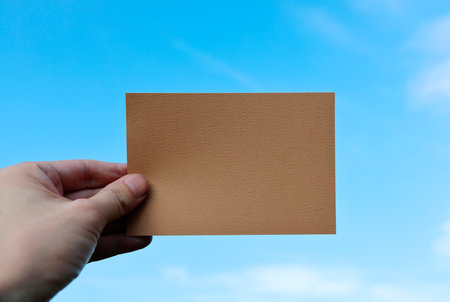 Hand holding brown card on blue sky background. Copy space.の写真素材