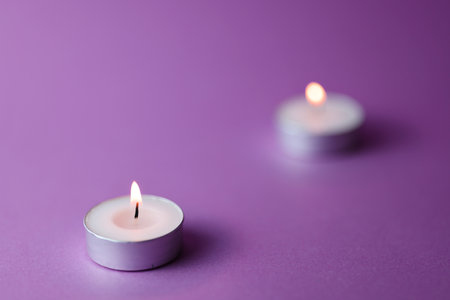 Two burning candles on purple background, closeup. Space for textの写真素材