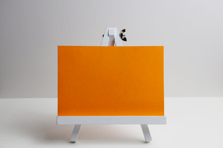 White easel with orange canvas on white background. Mockup for designの写真素材