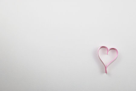 Pink ribbon in the shape of a heart on a white background.の写真素材
