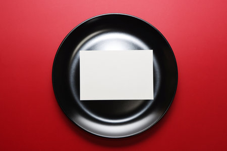 Blank white card on a black plate on a red background.の写真素材