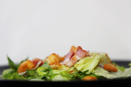 Salad with bacon on a black plate isolated on white backgroundの写真素材