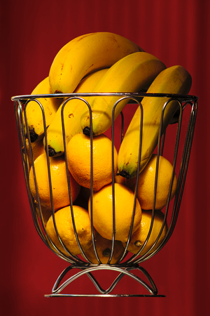 Bananas and oranges in metal basket with garnet curtain as backgroundの写真素材