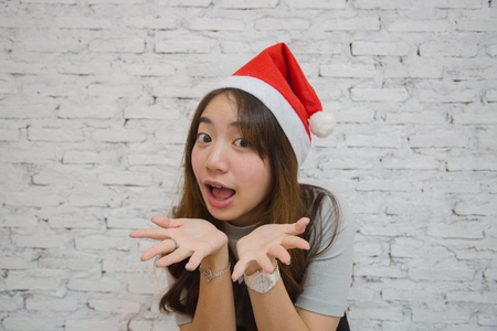 Young asian woman smiling and wearing christmas hat, on white brick backgroundの写真素材