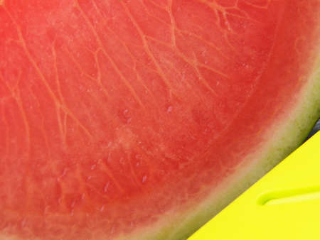 A large wartermelon fruit with texture details section and a yellow giant knife close-up. Fruit and utensil high angle viewの写真素材