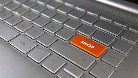 The word SHOP on an orange button on a silver laptop keyboardの写真素材