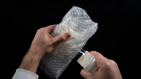 Packing with bubble plastic wrap and duct tape, package for shipping, male hands wrapping, isolated...