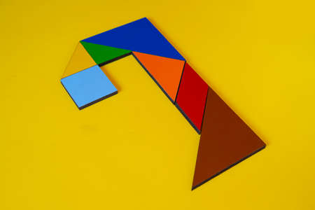 Colorful tangram puzzle in the shape of a arrow on yellow background