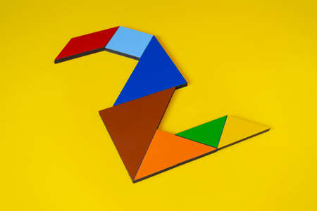 Paper tangram puzzle in red, orange, blue and green colors on yellow backgroundの写真素材
