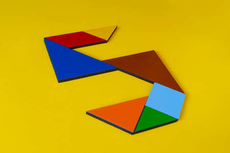 Colorful paper tangram puzzle in shape of arrow on yellow backgroundの写真素材