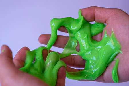 A child's hand squeezes slime on a white background, close-up.