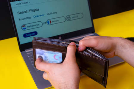 Man's hands holding a wallet and using a laptop.