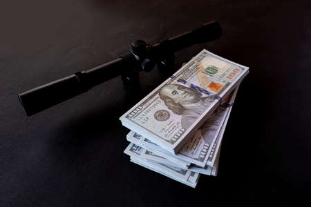 A bundle of dollars and a gun on a black background.