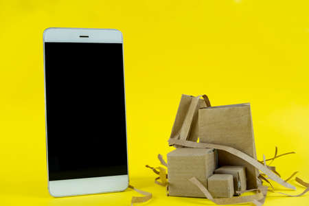 Smartphone with cardboard boxes on a yellow background. Copy space.