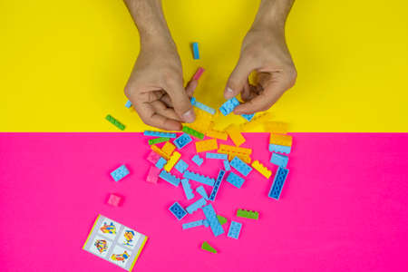 Male hands playing with multicolored plastic blocks on a pink and yellow background