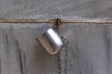 Old metal kettle hanging on a concrete wall with chain. Selective focus.