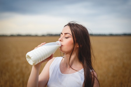 Beautiful woman is drinking milk in countrysideの写真素材