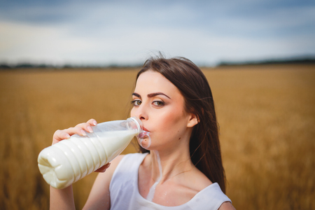 Beautiful woman is drinking milk in countrysideの写真素材
