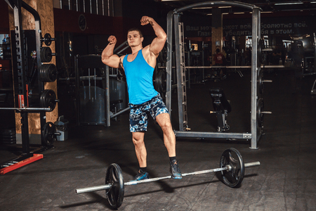 Man standing near heavy barbells in gym showing his musclesの写真素材
