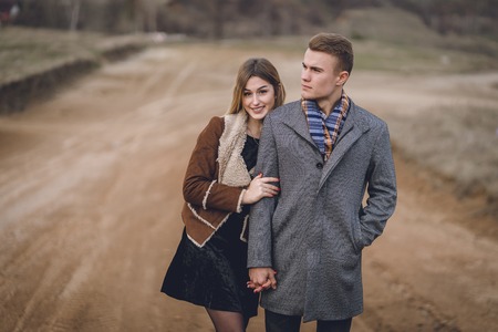 A nice beautiful lovely couple in the park or field or track. man in Gray coat and scarf with girl woman in brown coat. lovers walking hold hands. put her head on his shoulder hugged behindの写真素材