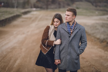 A nice beautiful lovely couple in the park or field or track. man in Gray coat and scarf with girl woman in brown coat. lovers walking hold hands. put her head on his shoulder hugged behindの写真素材