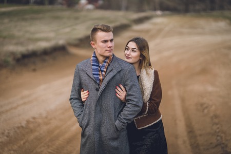 A nice beautiful lovely couple in the park or field. man in Gray coat and scarf with girl woman in brown coat. lovers walking hold hands. put her head on his shoulder hugged behindの写真素材