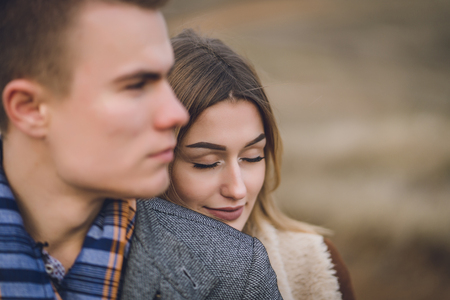 A nice beautiful lovely couple in the park or field. man in Gray coat and scarf with girl woman in brown coat. lovers walking hold hands. put her head on his shoulder hugged behindの写真素材